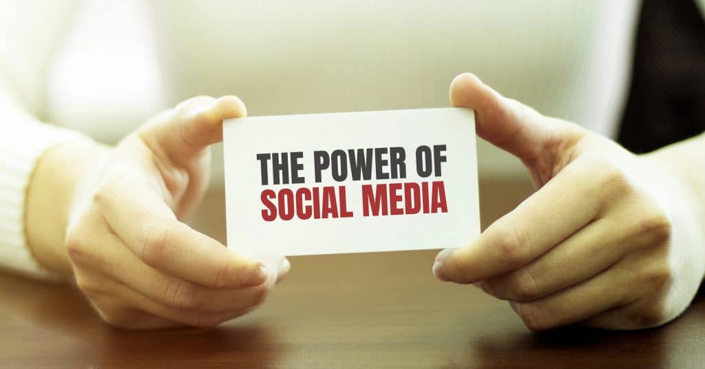 A person holds a card reading "The Power of Social Media" on a wooden table, emphasizing the impact and influence that effective social media management can unlock.