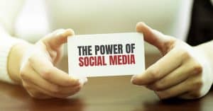 A person holds a card reading "The Power of Social Media" on a wooden table, emphasizing the impact and influence that effective social media management can unlock.